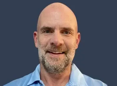 A bald man with a beard is smiling for the camera while wearing a blue shirt.