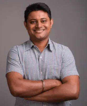 A man in a plaid shirt is standing with his arms crossed and smiling.