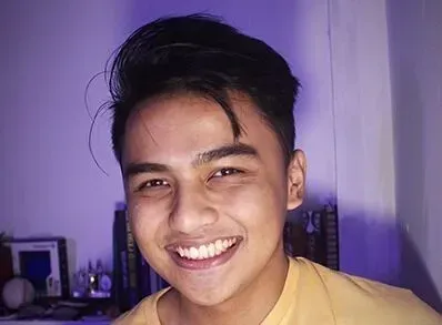 A young man in a yellow shirt is smiling for the camera.