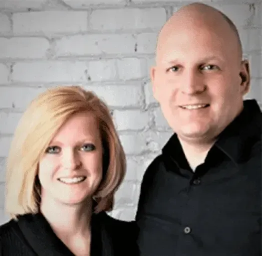 A man and a woman are posing for a picture in front of a white brick wall.