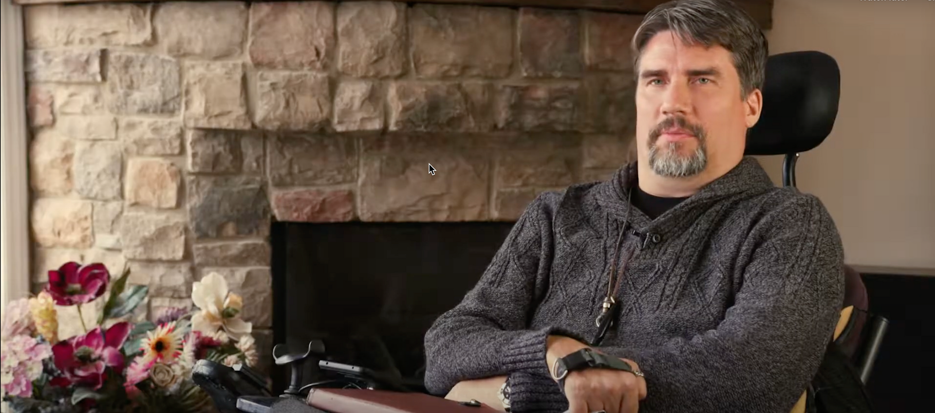 A man in a wheelchair is sitting in front of a fireplace.