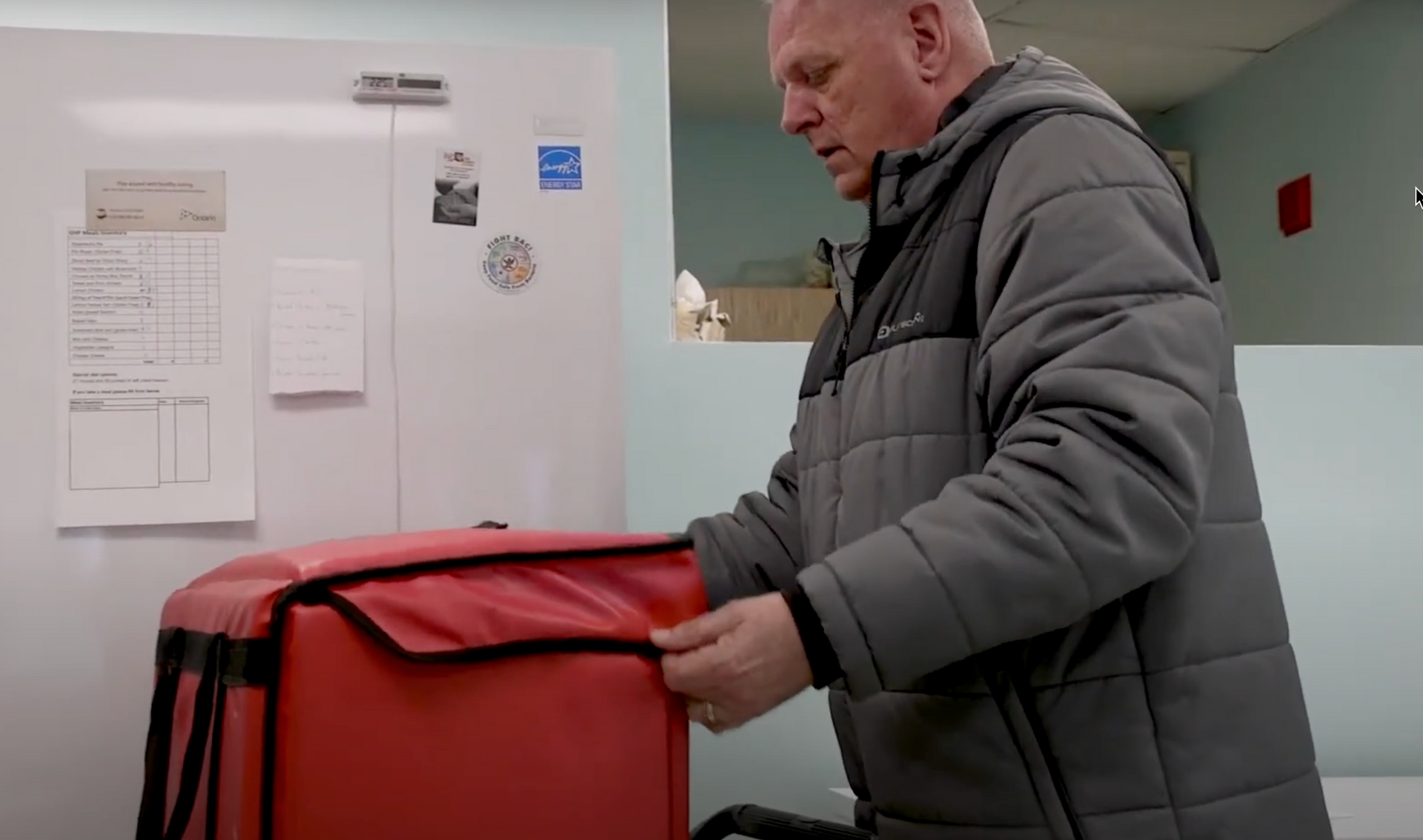 A man in a gray jacket is holding a red bag.