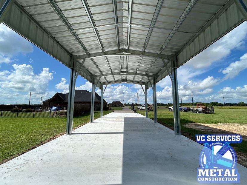 Covered metal walkway with a concrete path under a roof, beside a grassy field under a blue sky.