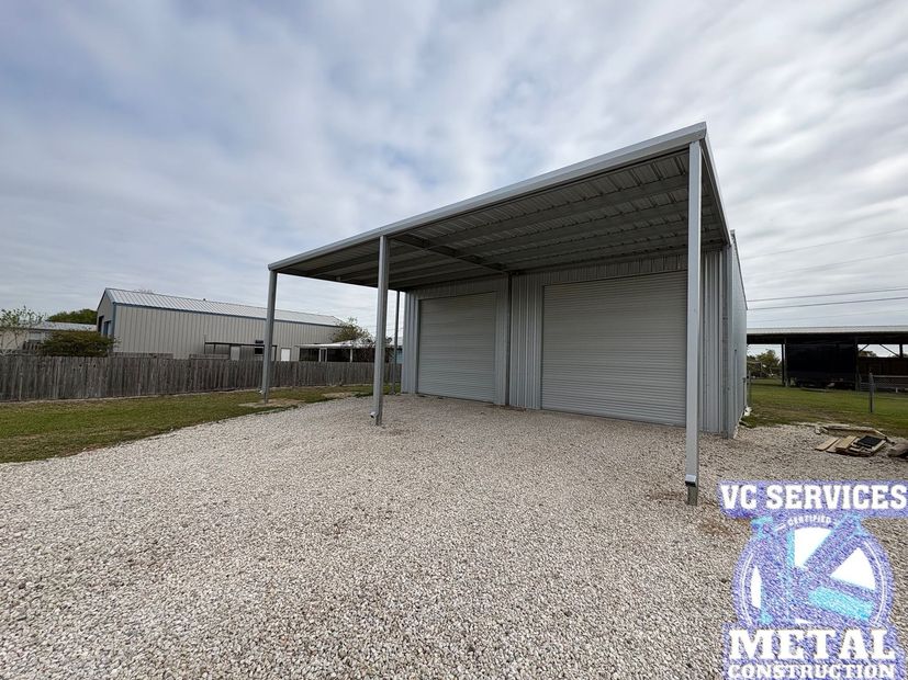 Metal carport with gravel ground and a corrugated metal building under an overcast sky.