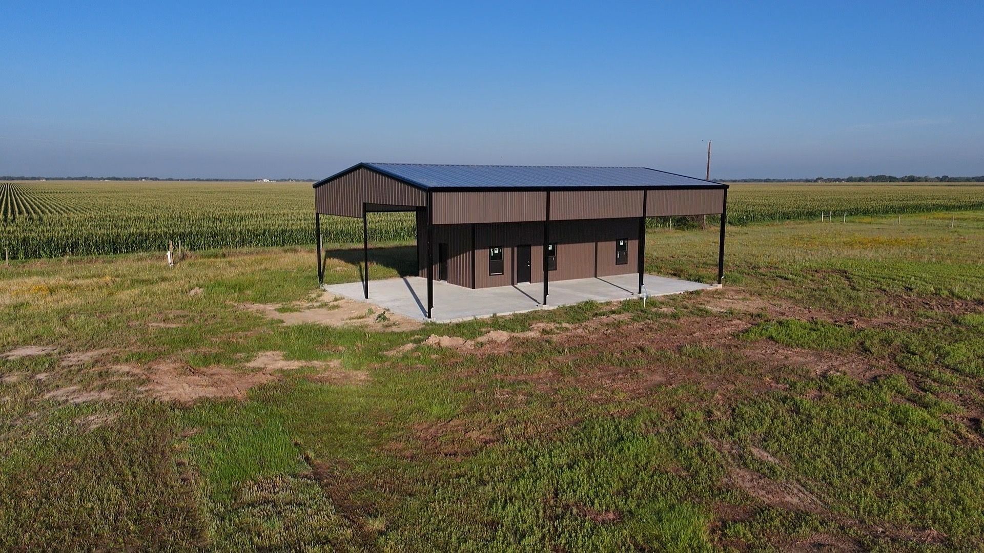 Small metal shed with a dark roof in a grassy field beside a cornfield under a clear sky