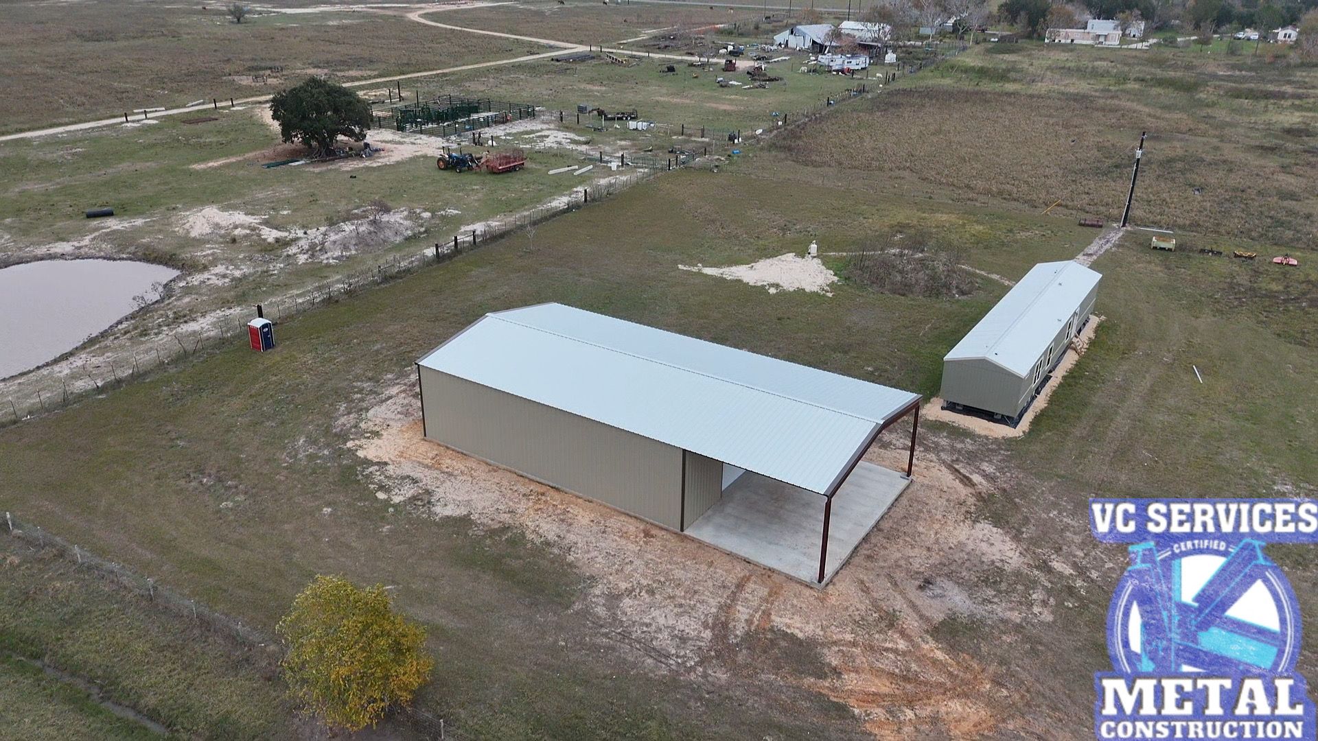 Aerial view of two metal sheds on a grassy rural lot with dirt paths and open fields.