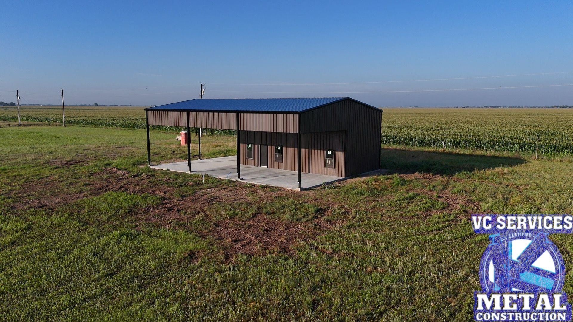 Small black metal shed with a blue roof on a concrete slab in a grassy field under a clear sky.