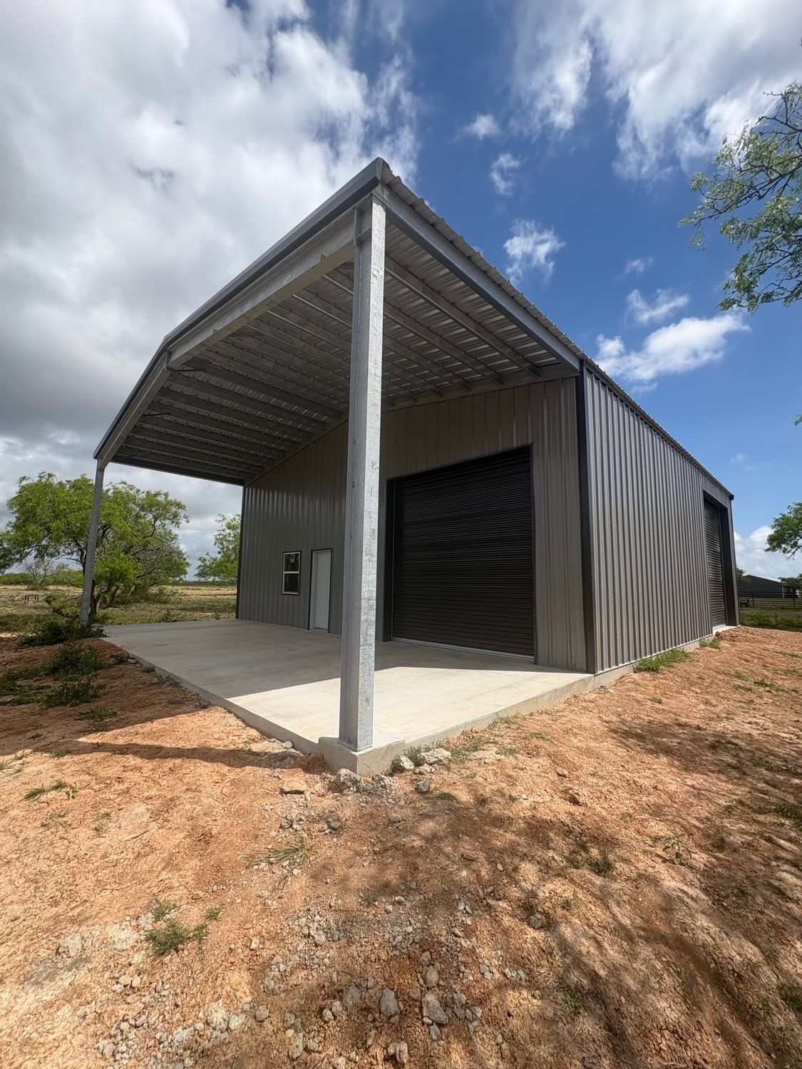 Small modern metal shed with open porch and ramp on a dirt lot under a cloudy sky