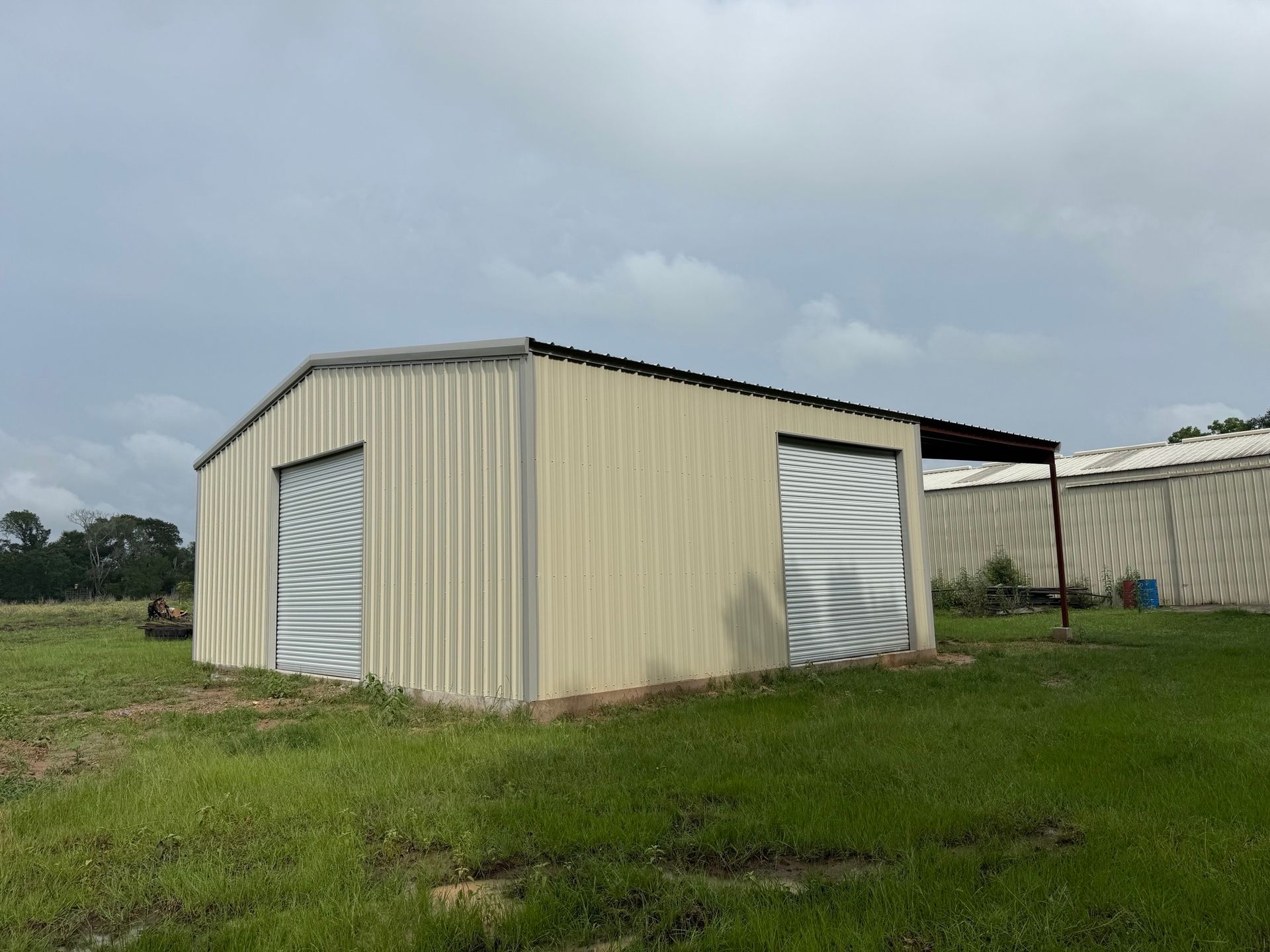 Small beige metal shed with white doors on a grassy field under a cloudy sky