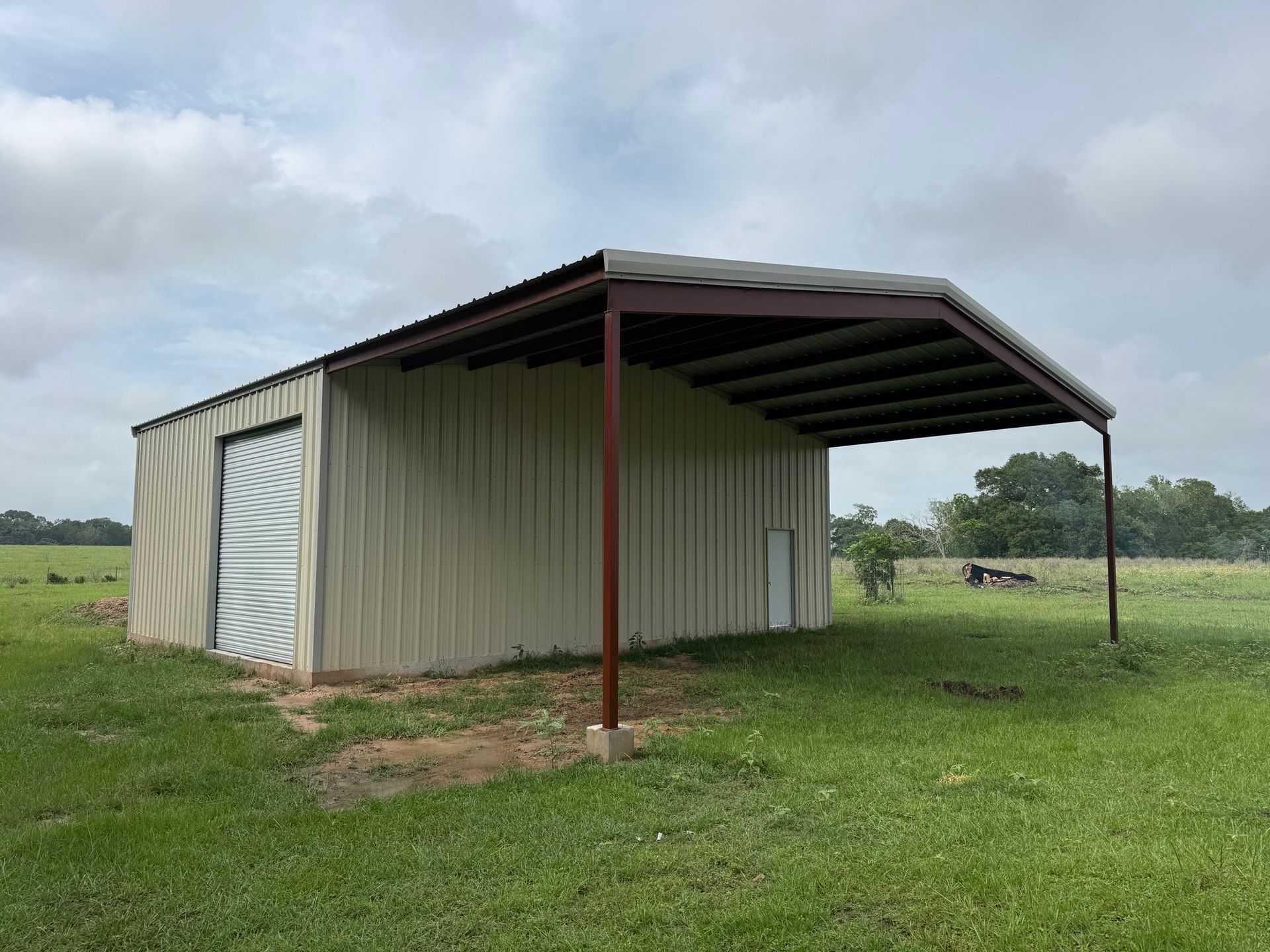 Small metal shed with a covered overhang on a grassy field under cloudy sky
