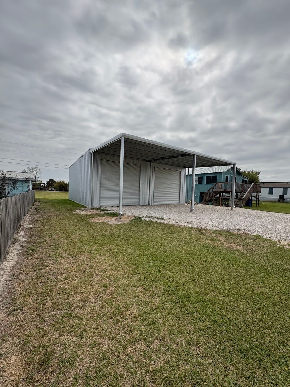 Gravel lot with a metal carport beside a blue camper under a cloudy sky