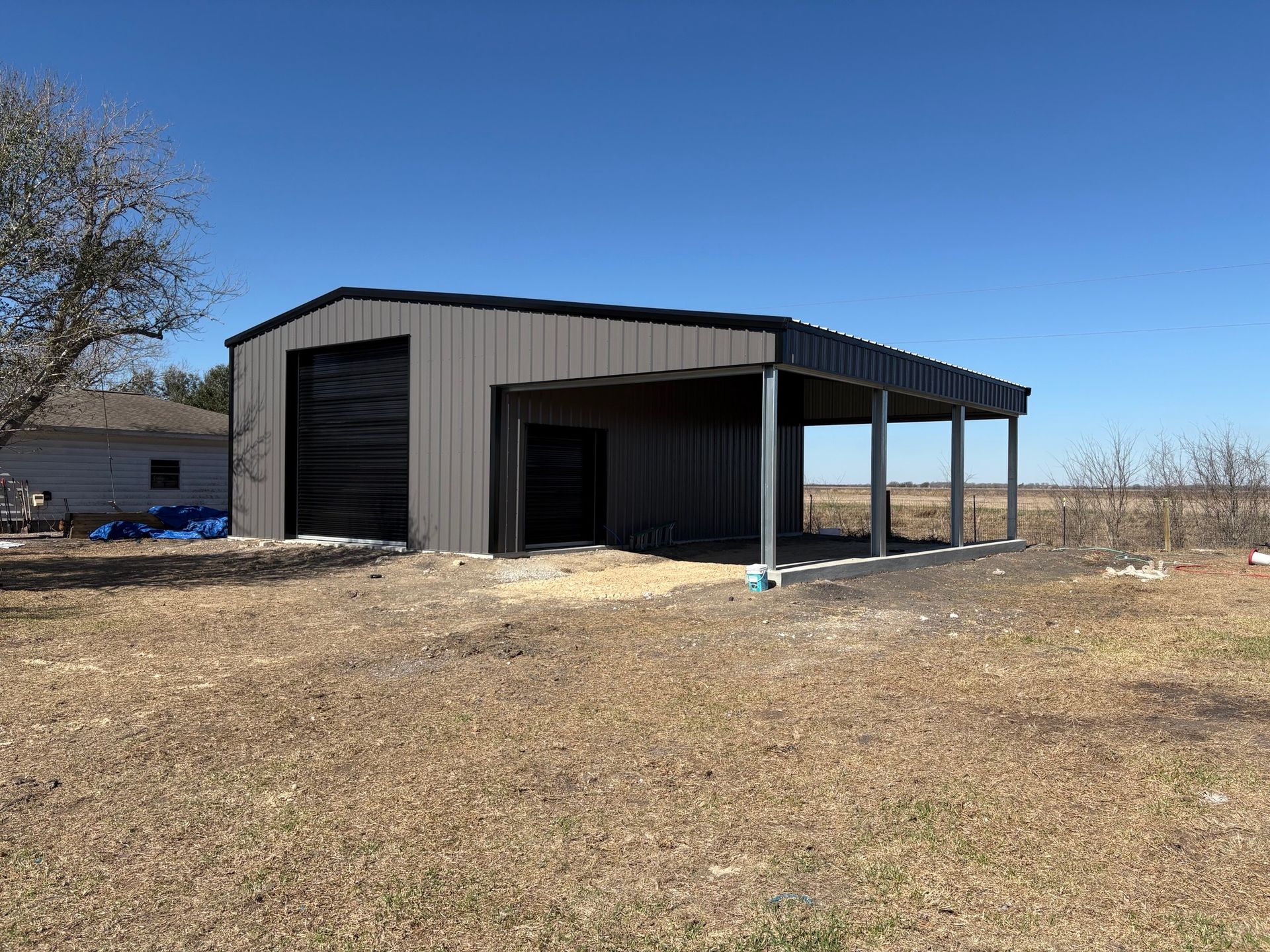Metal storage building with a covered porch in a dry open field under a clear blue sky