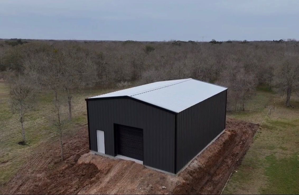 Black metal barn with white roof on a dirt lot in a wooded rural area