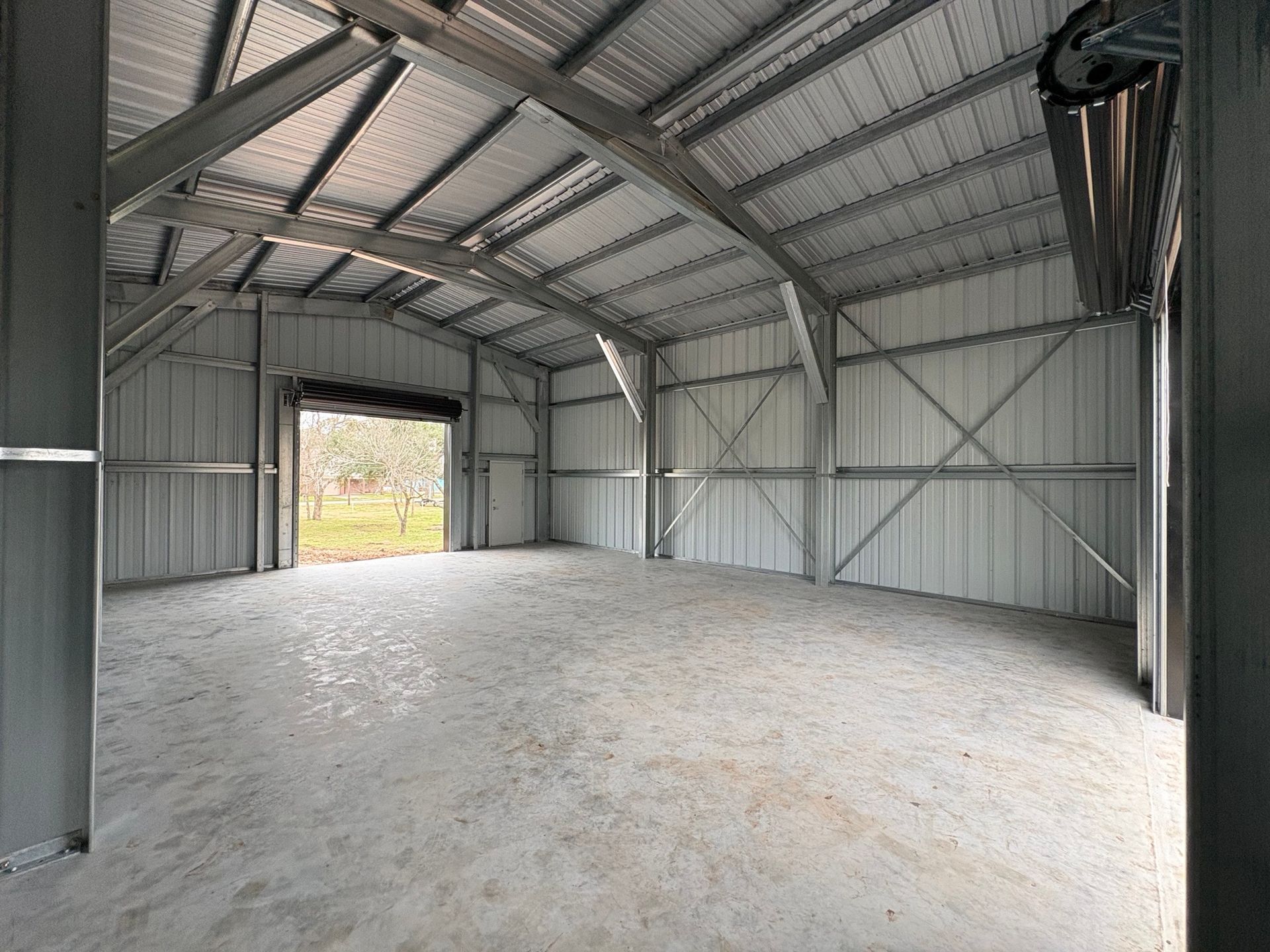 Empty metal shed interior with concrete floor and open doorway to the outdoors
