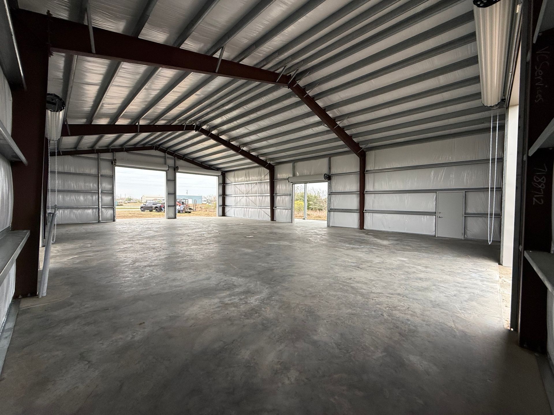 Empty industrial warehouse with metal walls, concrete floor, and large open doorway.