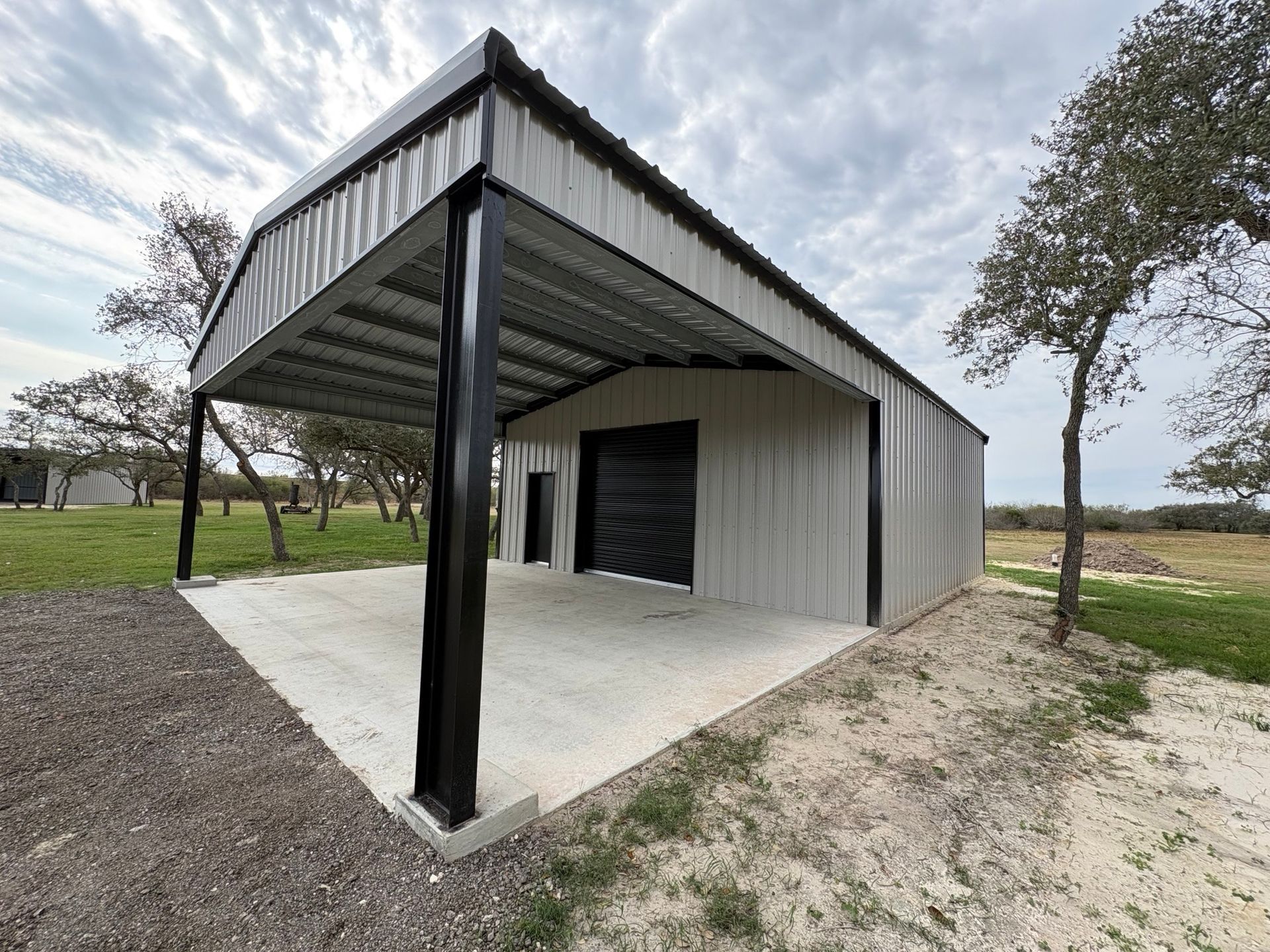 Modern metal pavilion with a black post, corrugated roof, and gravel driveway in a rural setting