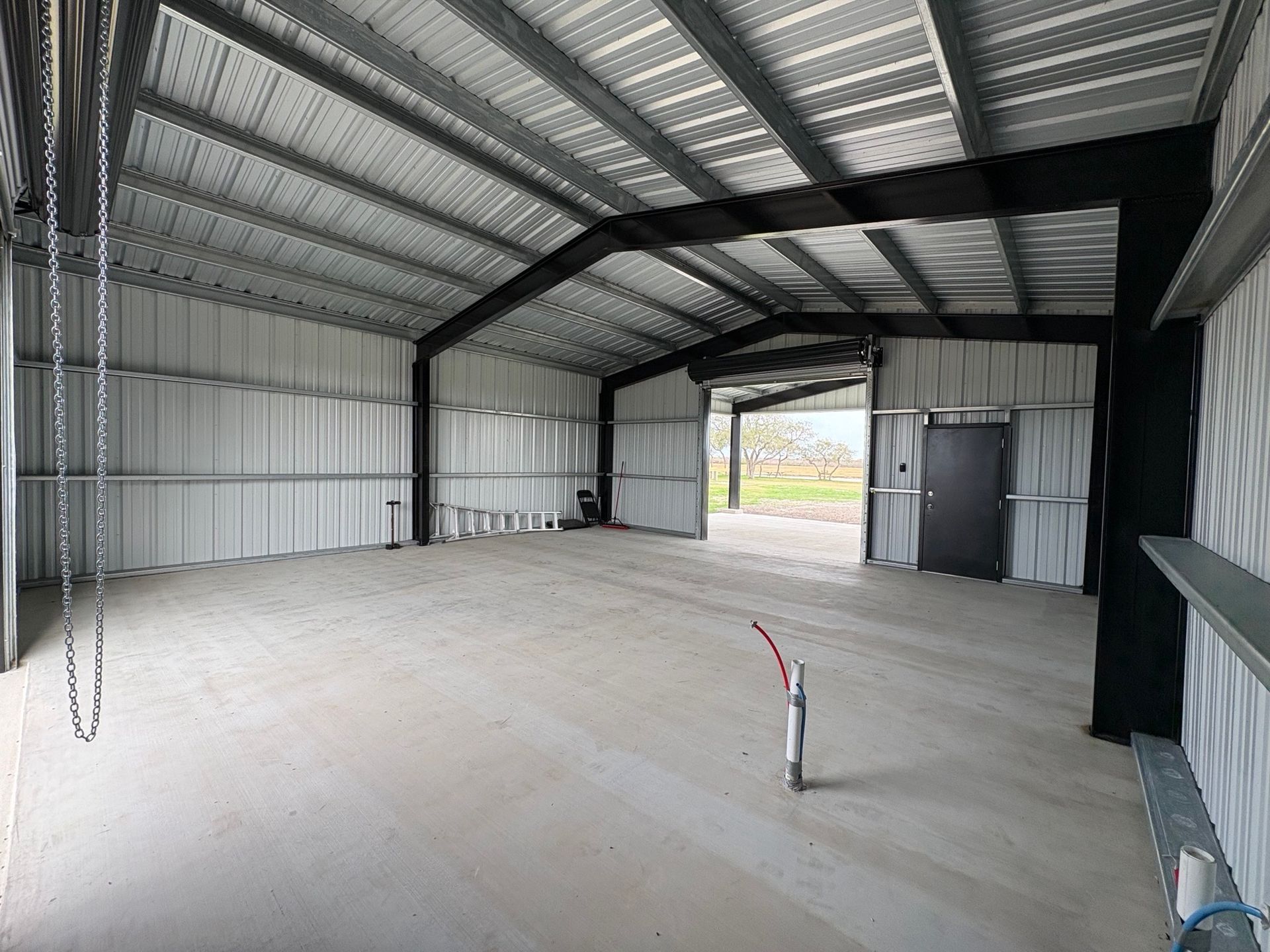 Empty metal warehouse interior with concrete floor, exposed beams, and open doorway to daylight