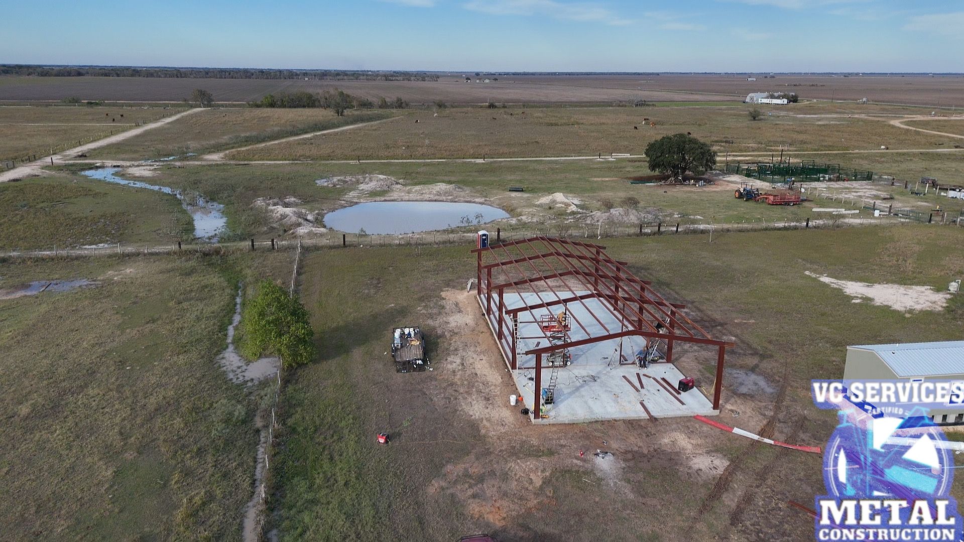 Aerial view of a rural flooded field with a metal building frame and a work vehicle nearby.