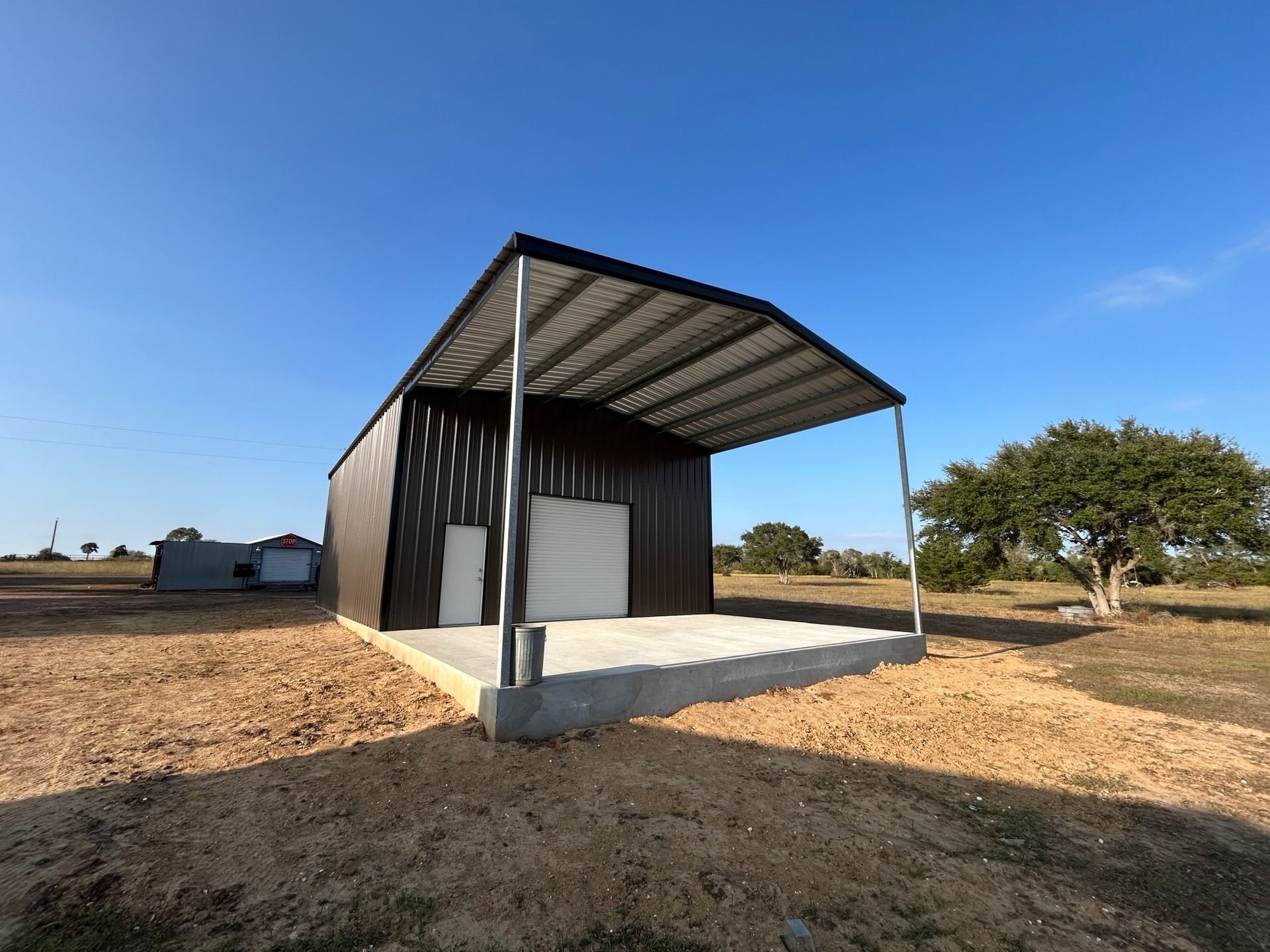 Small corrugated metal shed with an open front on a concrete slab in a dry rural field under blue sky