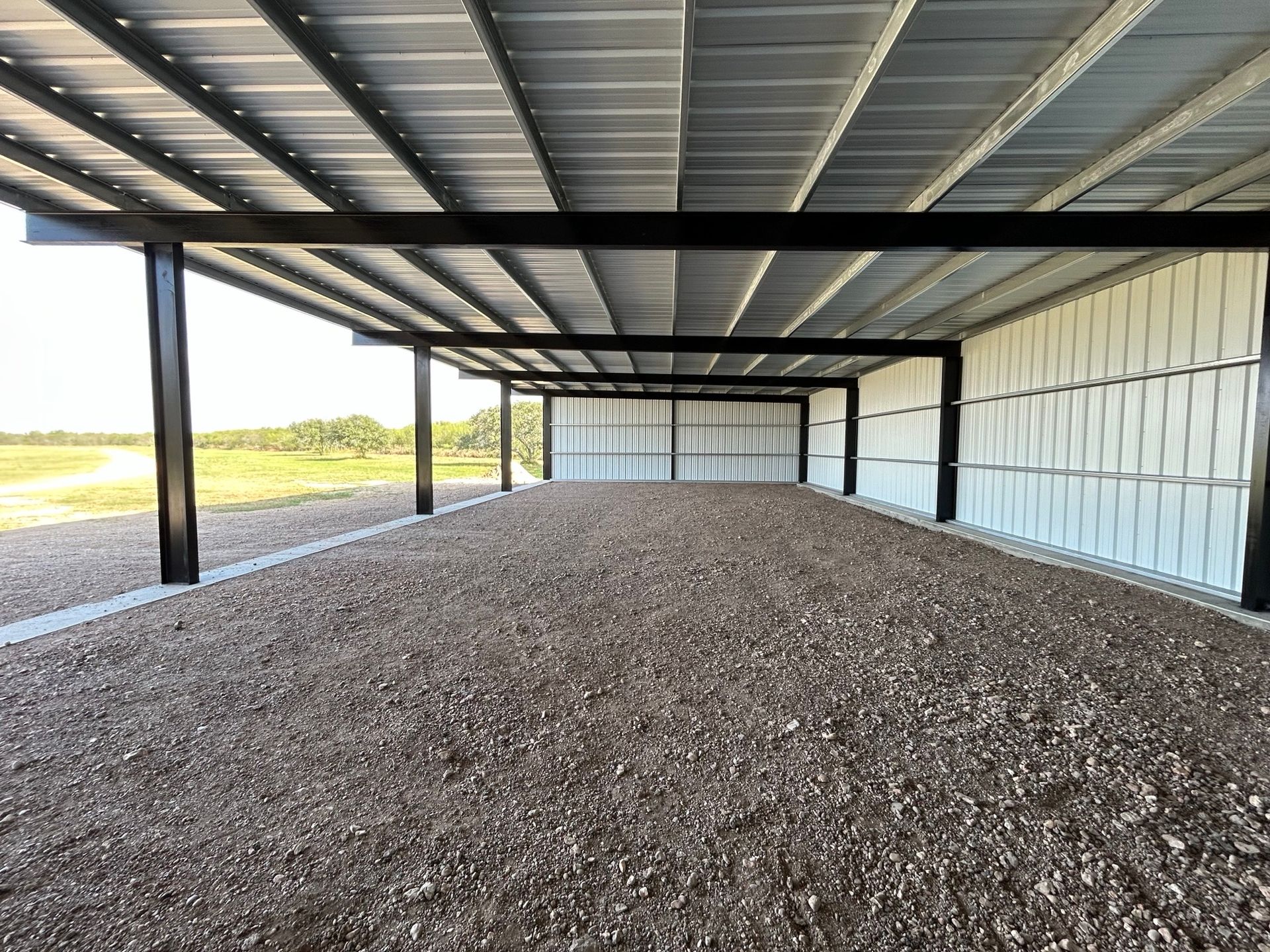 Covered gravel storage bay with steel beams and white wall panels, viewed from one end.