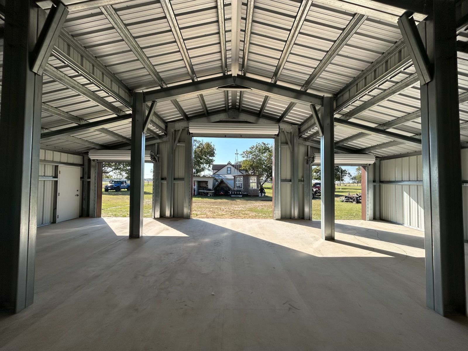 Empty metal carport interior with concrete floor and view of houses and trees outside