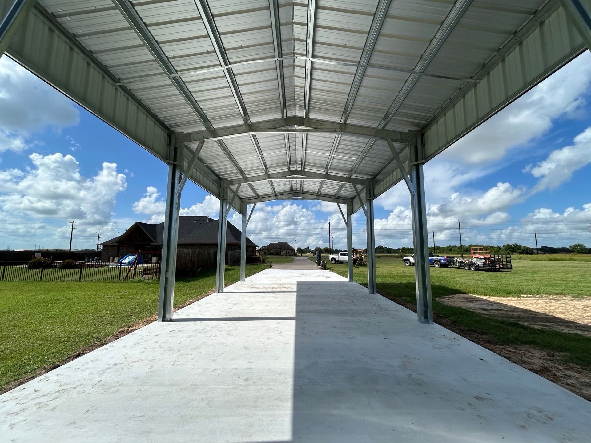 Covered concrete walkway with a metal roof in an open grassy field under a blue sky