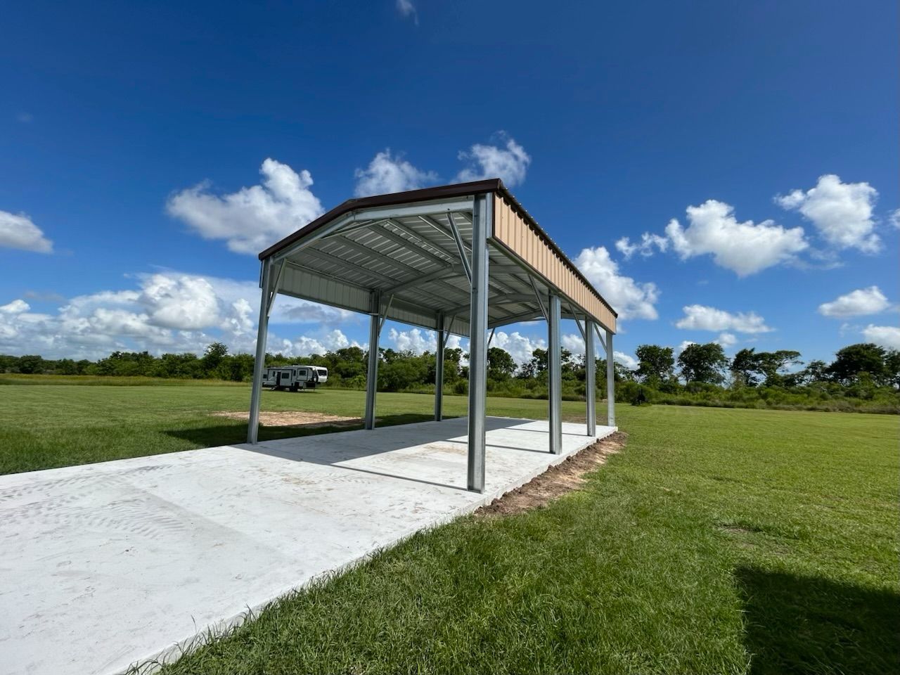 Open-sided metal shelter on a concrete pad in a grassy field under a blue sky with clouds