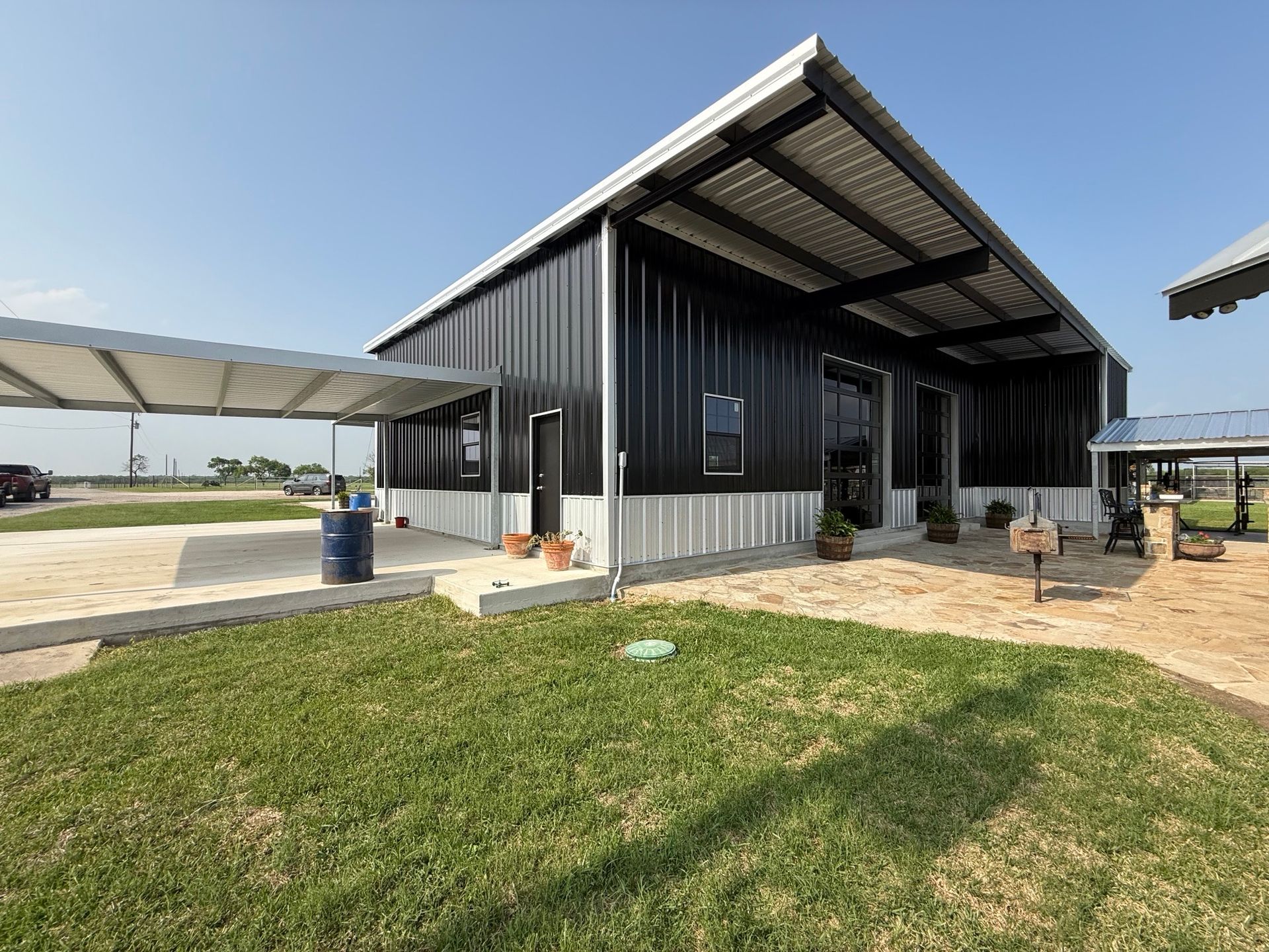 Black metal building with a covered entrance and grassy foreground under a clear blue sky