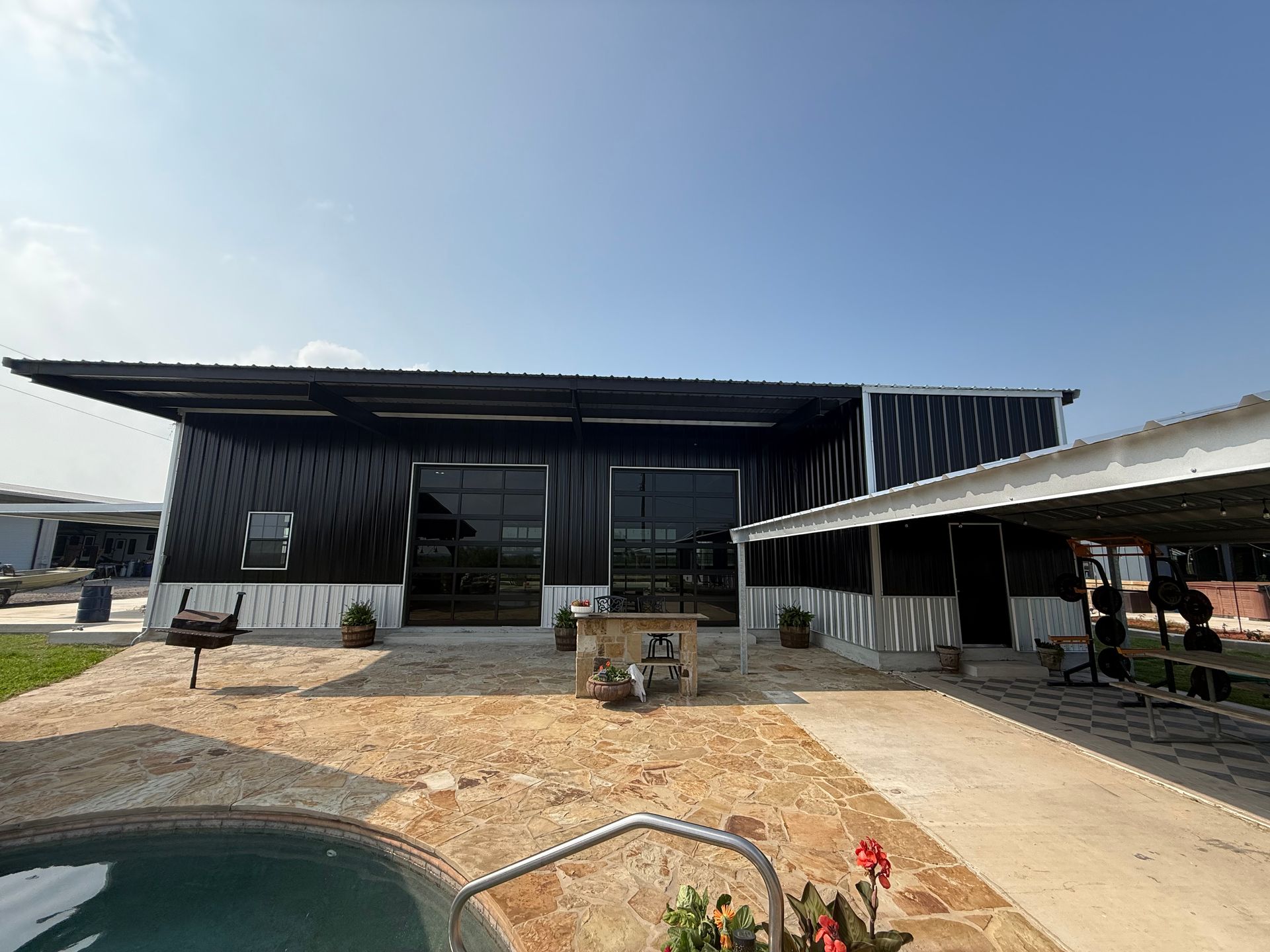 Modern black house with a pool, patio, and covered carport under a clear blue sky