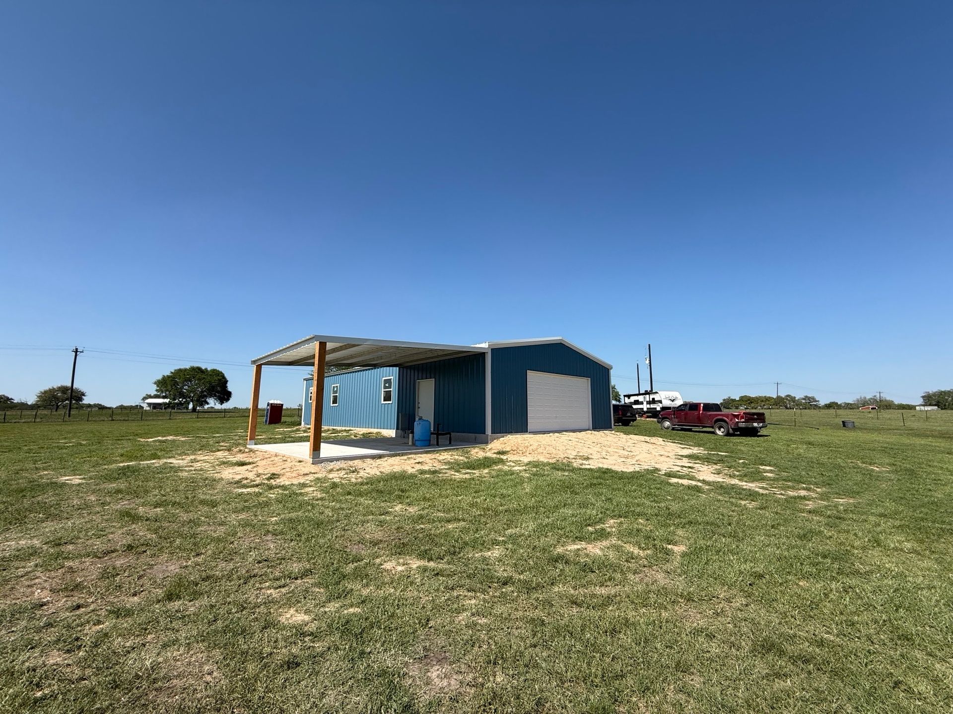 Small blue shed in a grassy field under a clear sky, with a red vehicle nearby.