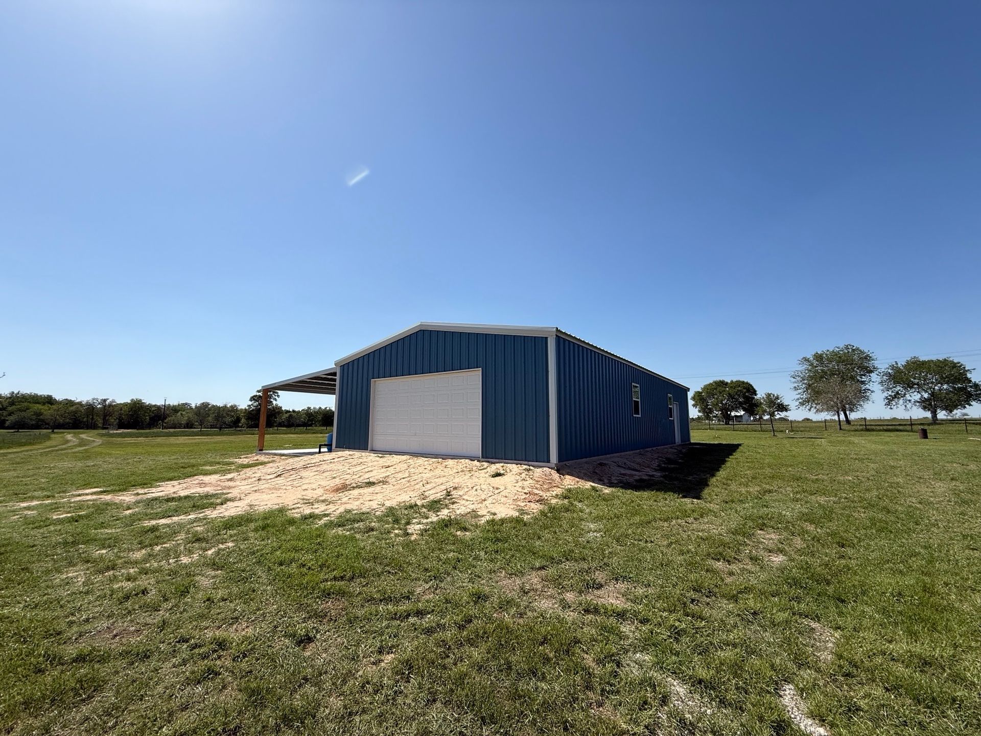 Blue metal shed on a grassy field under a clear sky, with a dirt mound in front.
