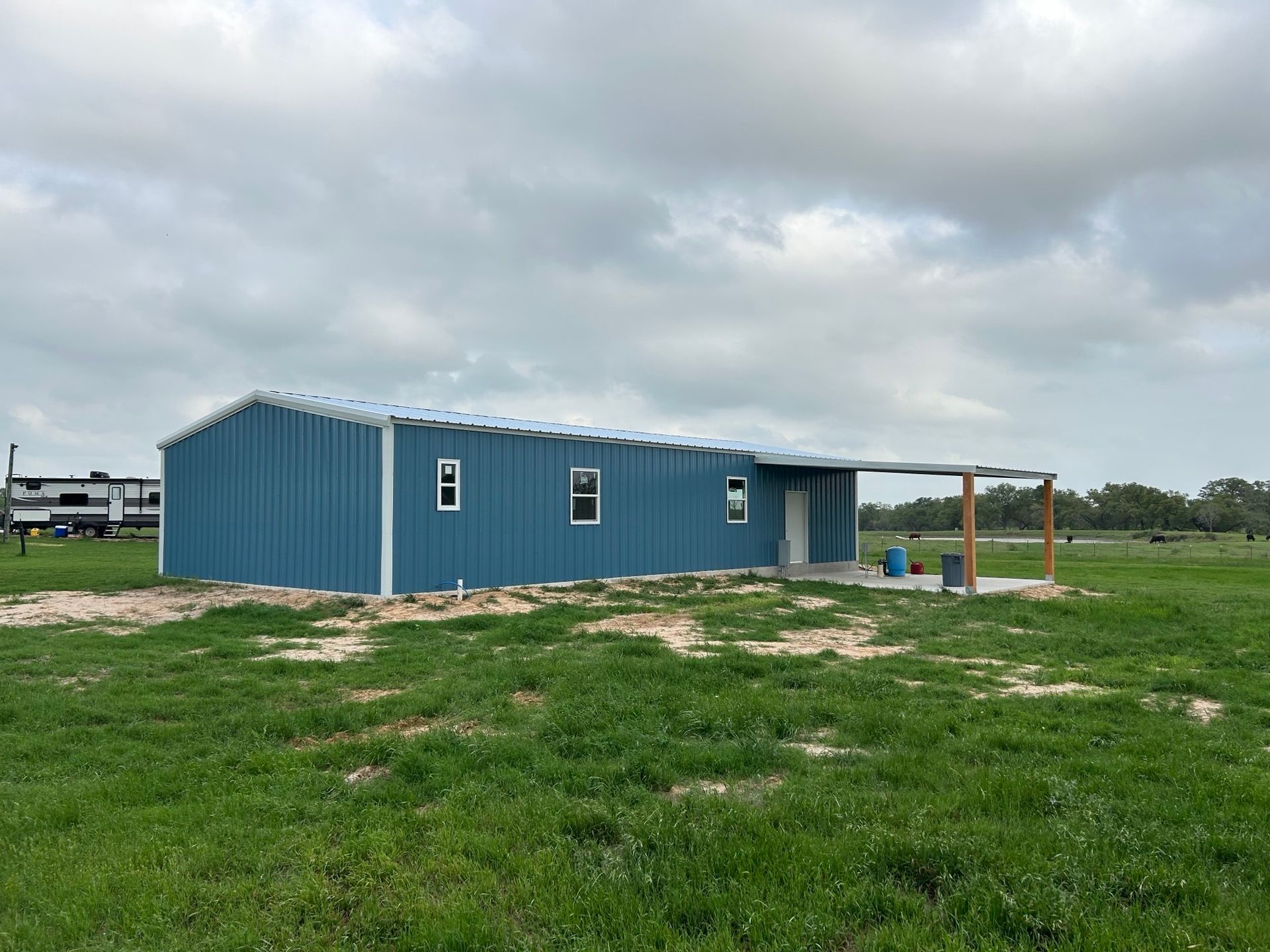 Blue metal building on a grassy lot under cloudy skies