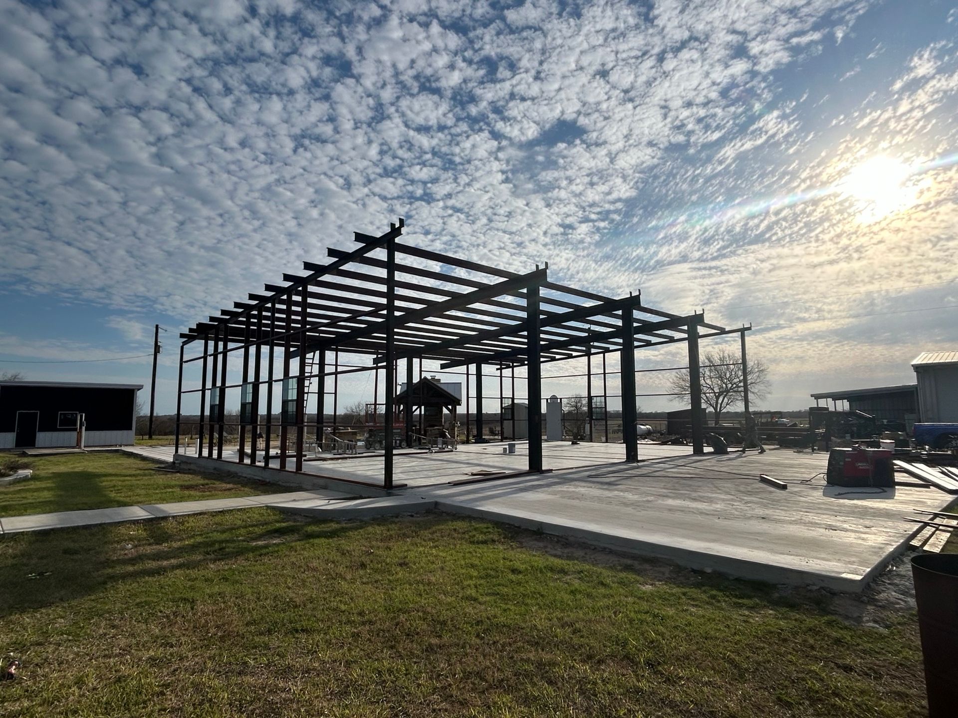Steel frame of a building under construction on a concrete slab in a grassy field at sunset