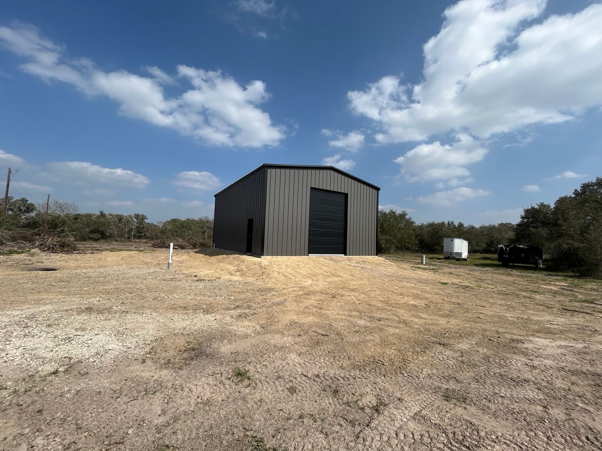 Small gray shed on a dry open field under a blue sky with clouds