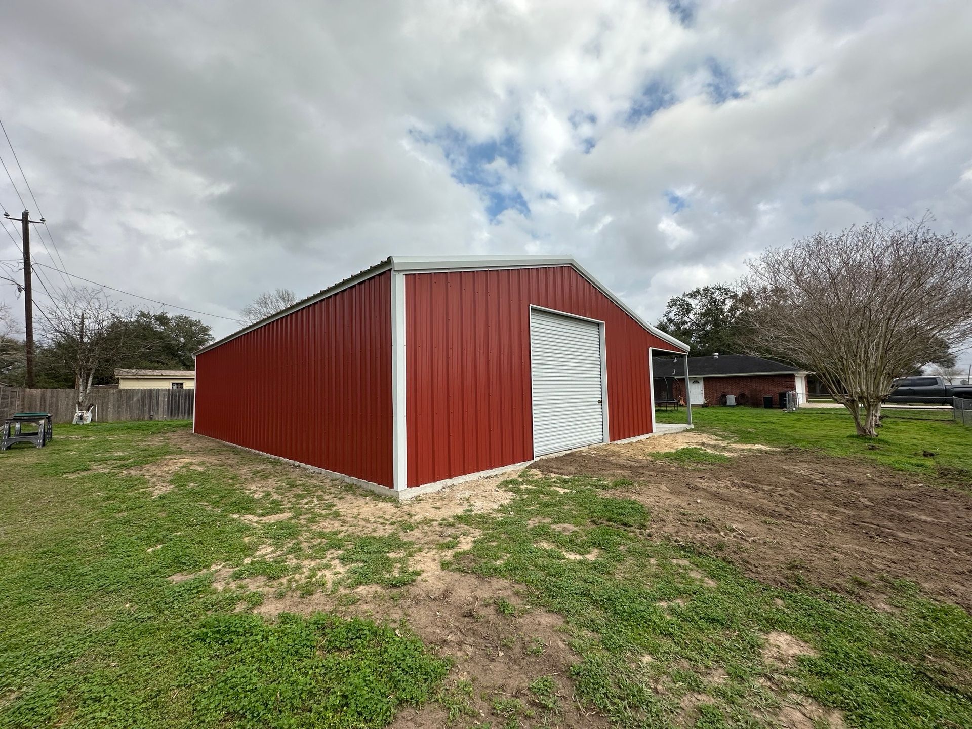 Red metal barn with a white door in a grassy rural yard under a cloudy sky