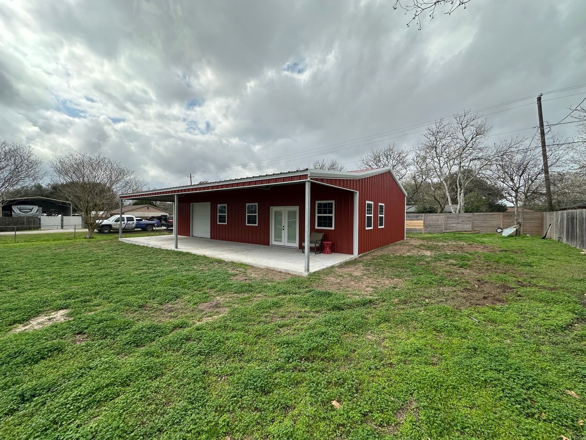 Small red house with a covered porch on a grassy lot under a cloudy sky