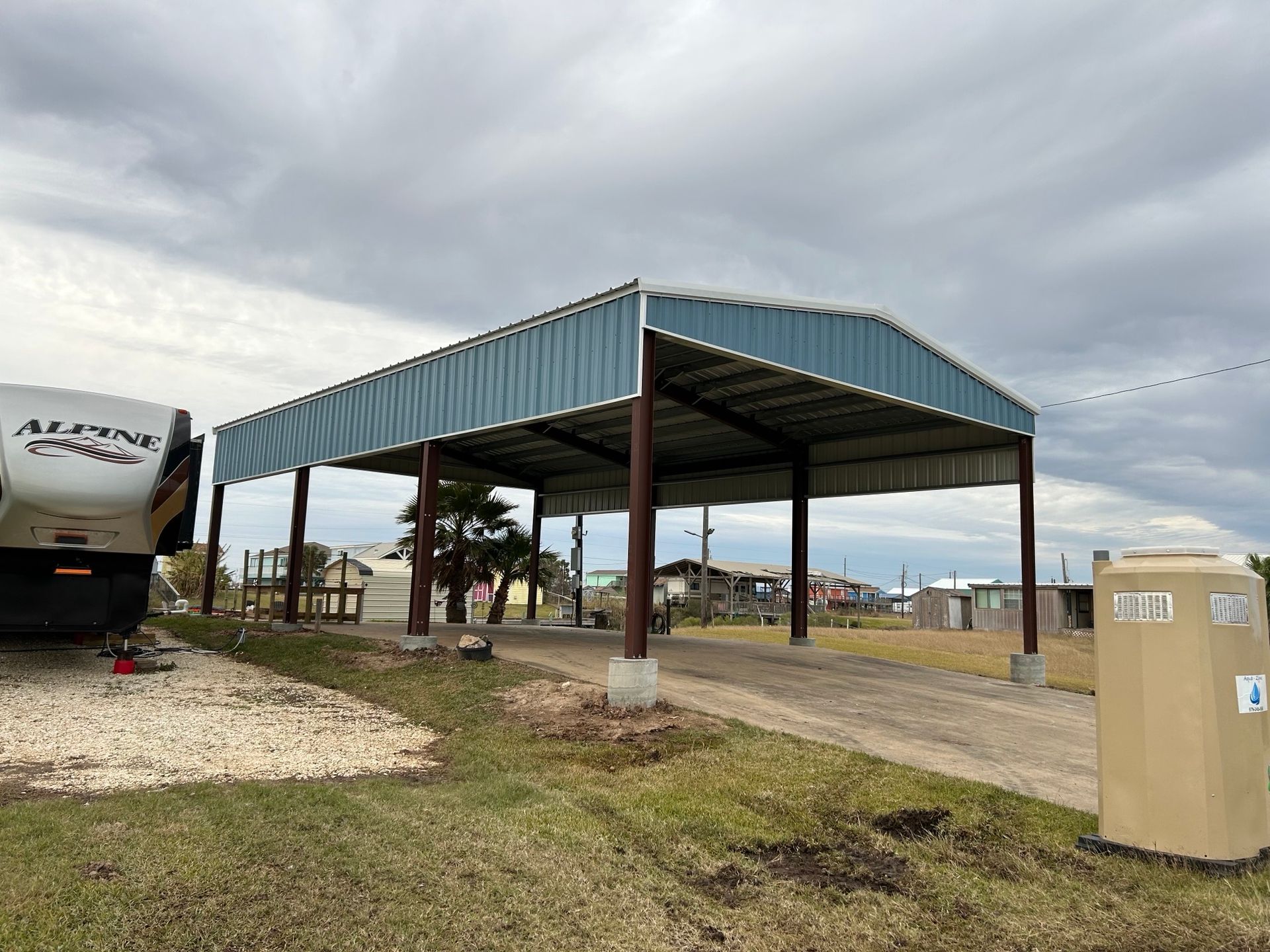Open-sided metal carport in a cloudy lot, with an RV on the left and a beige utility box on the right.