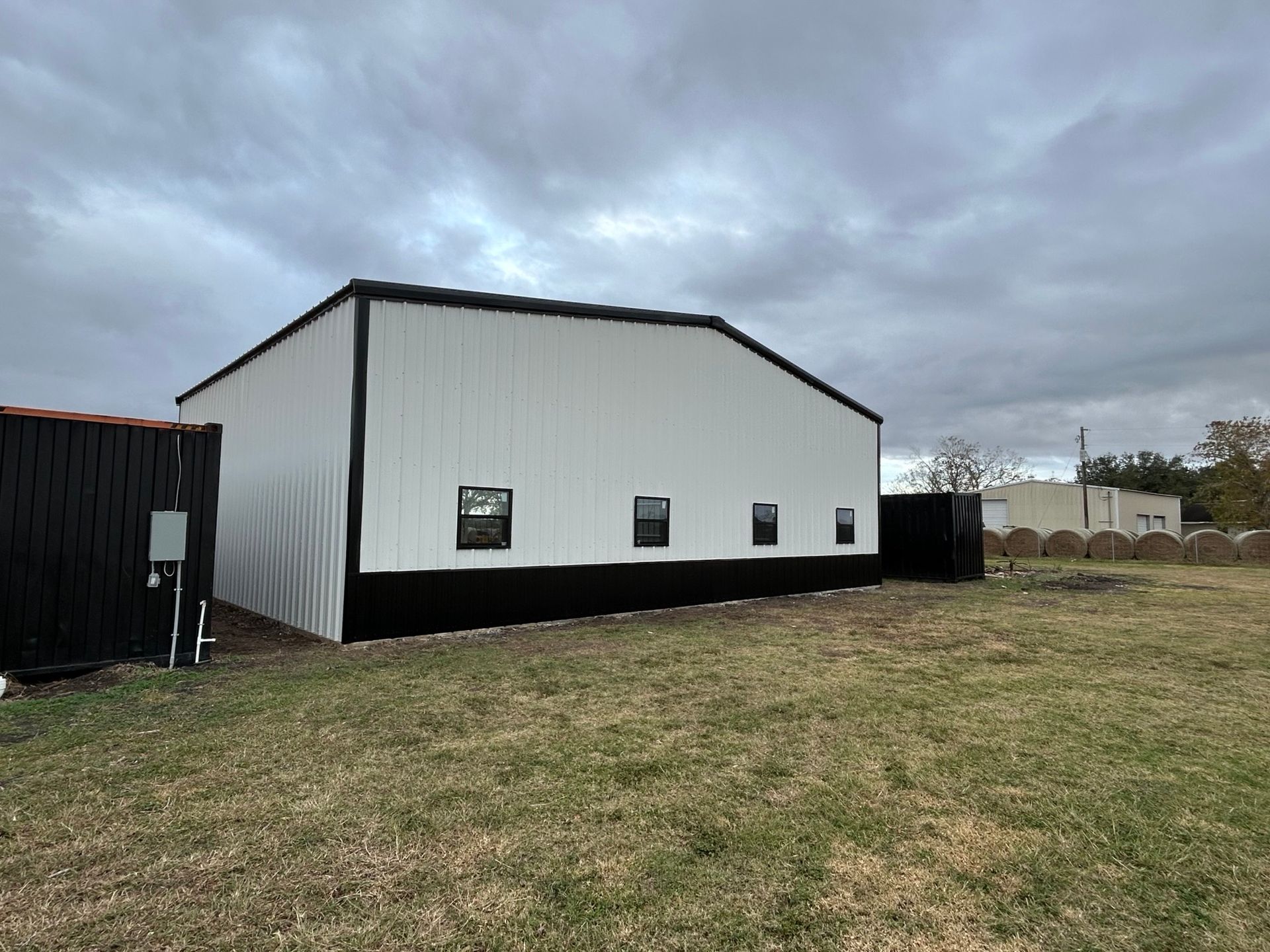 White metal barn with black trim in a grassy field under a cloudy sky.