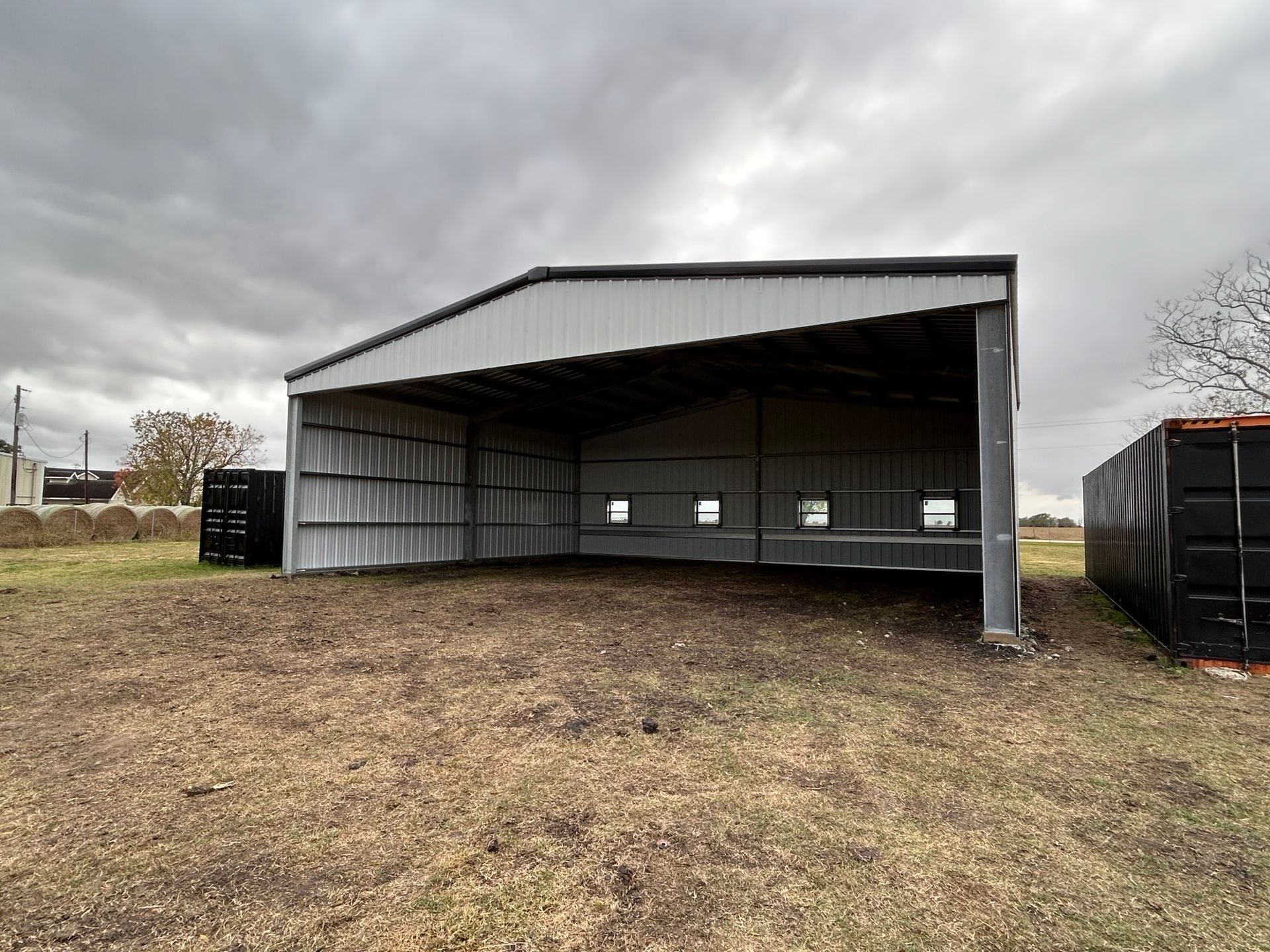 Open-sided metal shed on a grassy lot under a cloudy sky