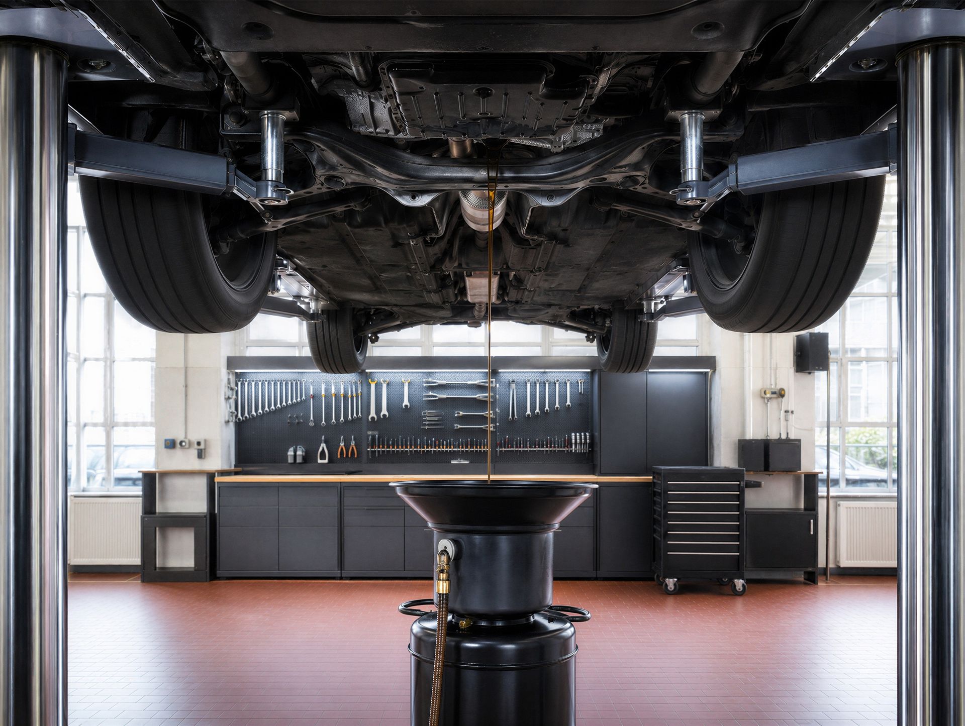 Car in a garage on a lift, viewed from below, with tool cabinets and workbench in the background Car in a garage on a lift, viewed from below, with tool cabinets and workbench in the background
