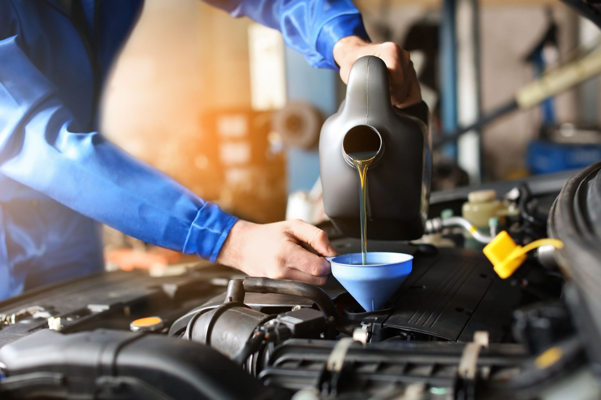 Mechanic pouring engine oil into a car through a funnel in an auto repair shop Mechanic pouring engine oil into a car through a funnel in an auto repair shop