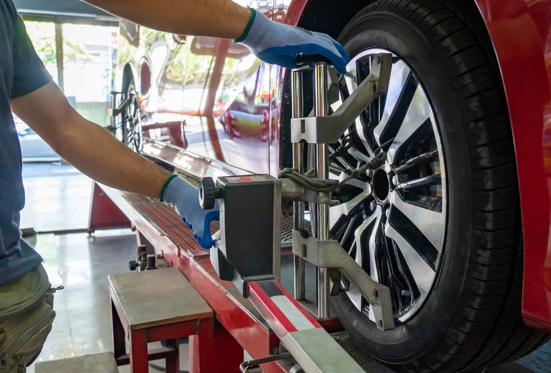 Mechanic using wheel alignment machine on a red car tire in a garage Mechanic using wheel alignment machine on a red car tire in a garage