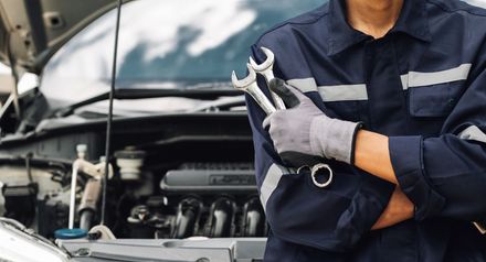 Mechanic in navy uniform holding wrenches beside an open car hood Mechanic in navy uniform holding wrenches beside an open car hood
