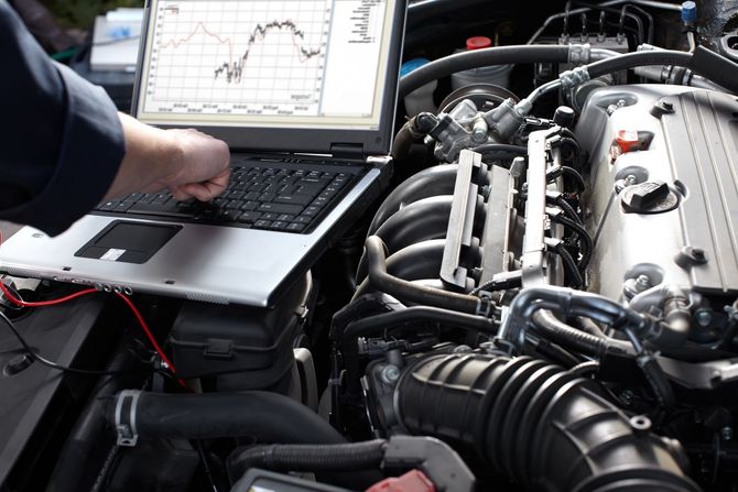 Mechanic using a laptop to diagnose a car engine in an open hood bay Mechanic using a laptop to diagnose a car engine in an open hood bay