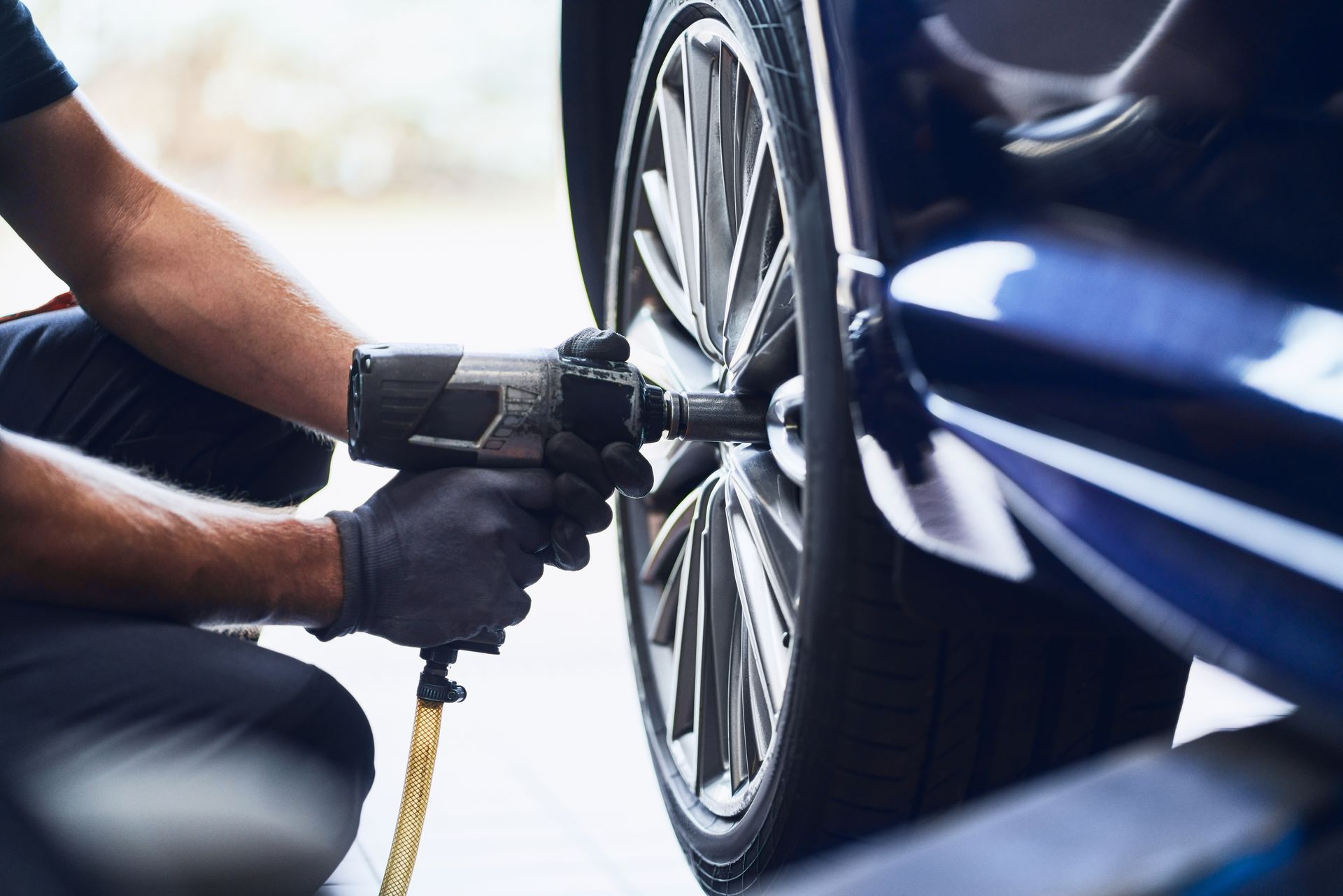 Mechanic using a power tool to remove a car wheel bolt on a blue vehicle Mechanic using a power tool to remove a car wheel bolt on a blue vehicle