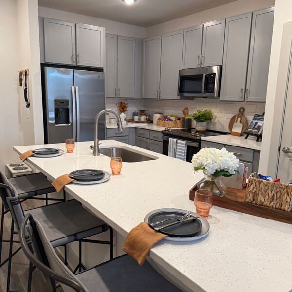 Modern white kitchen with island, stainless appliances, gray stools, and a flower centerpiece