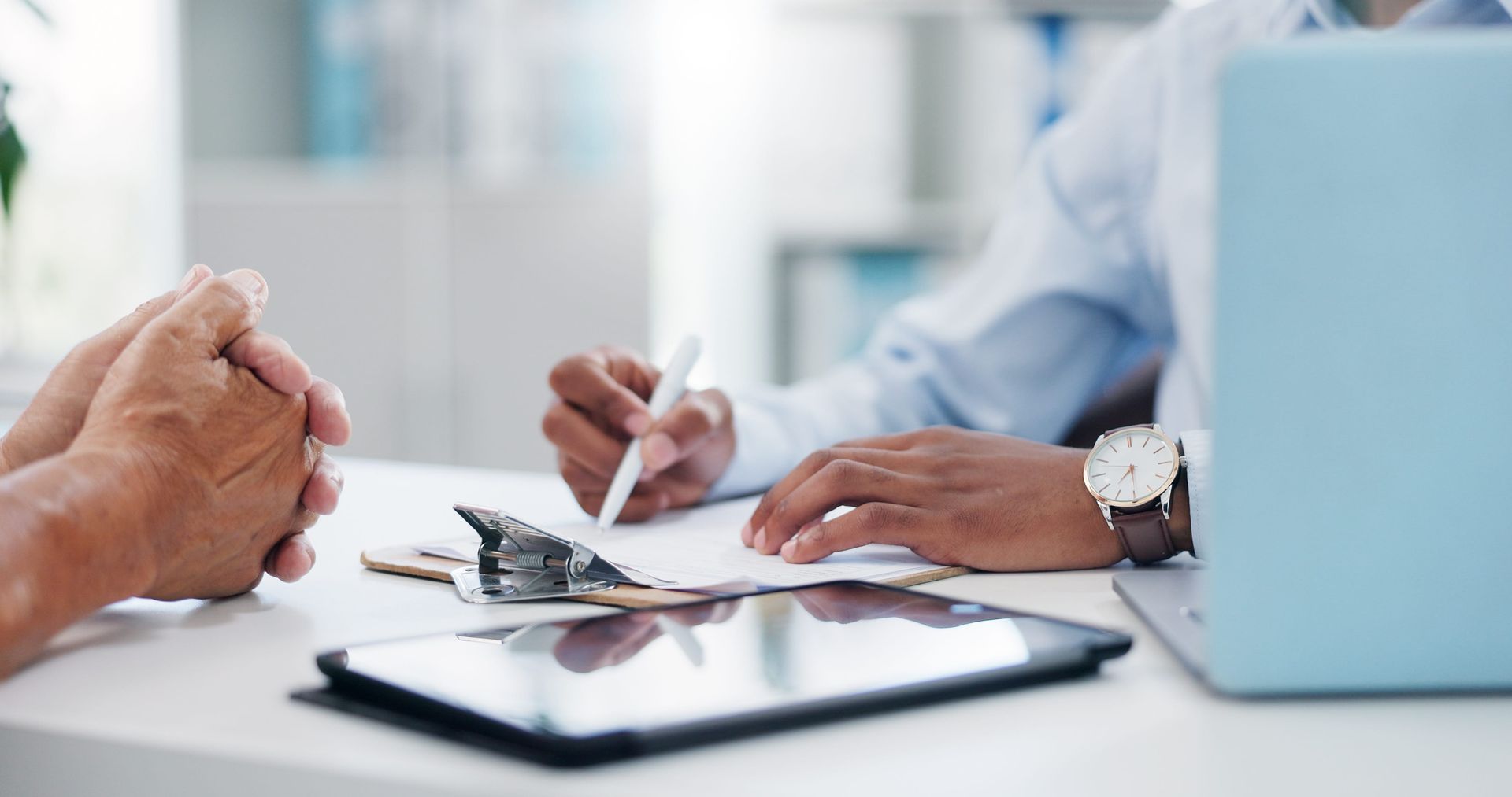 Business meeting with hands over documents, pen, and laptop on a desk