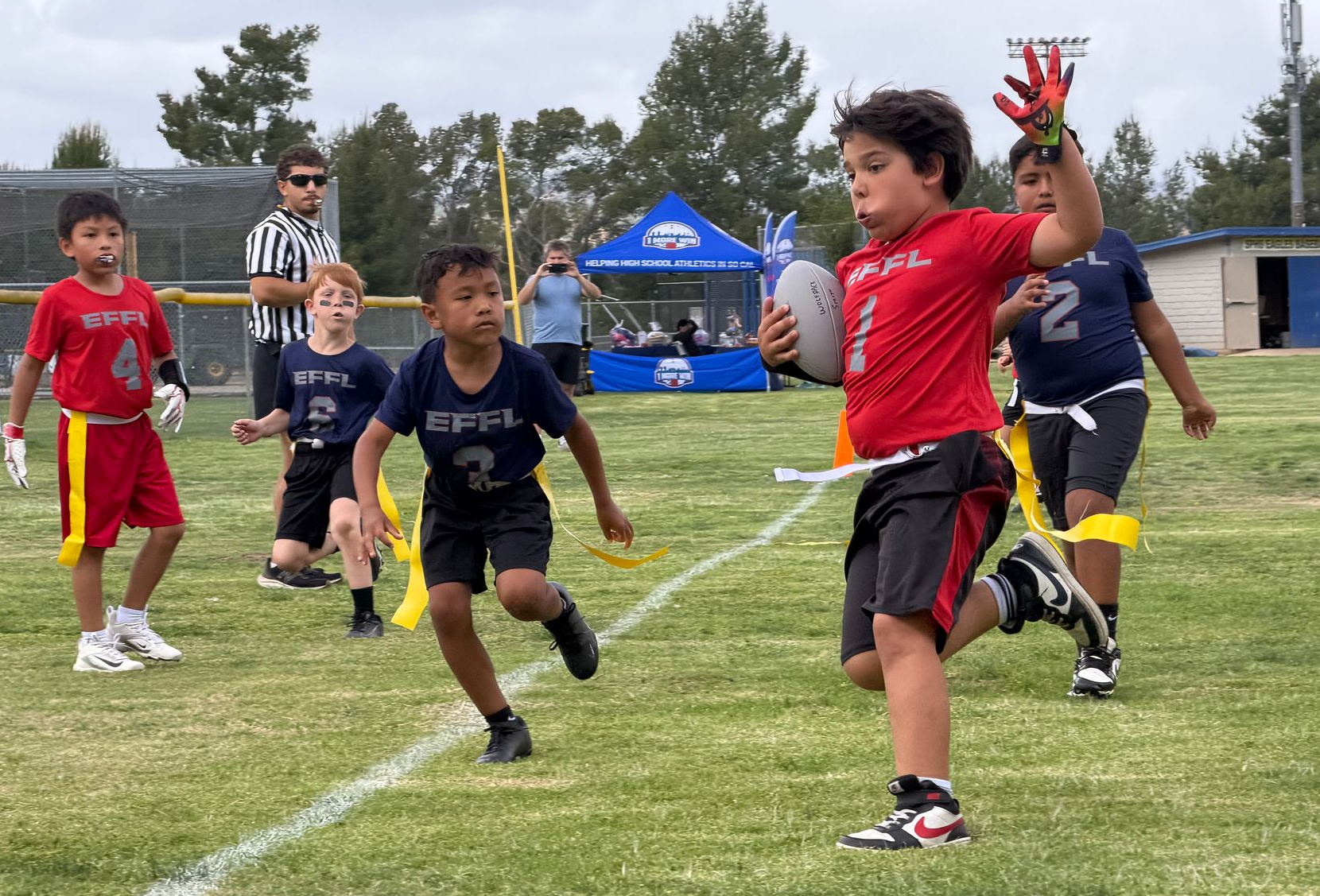 Youth flag football players sprint on a grassy field during a game.