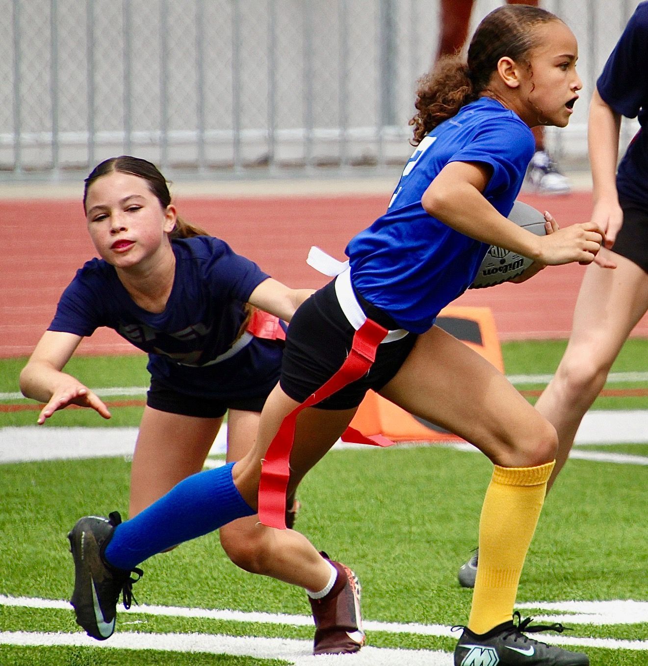 Children running in a relay race on a track, wearing blue uniforms.