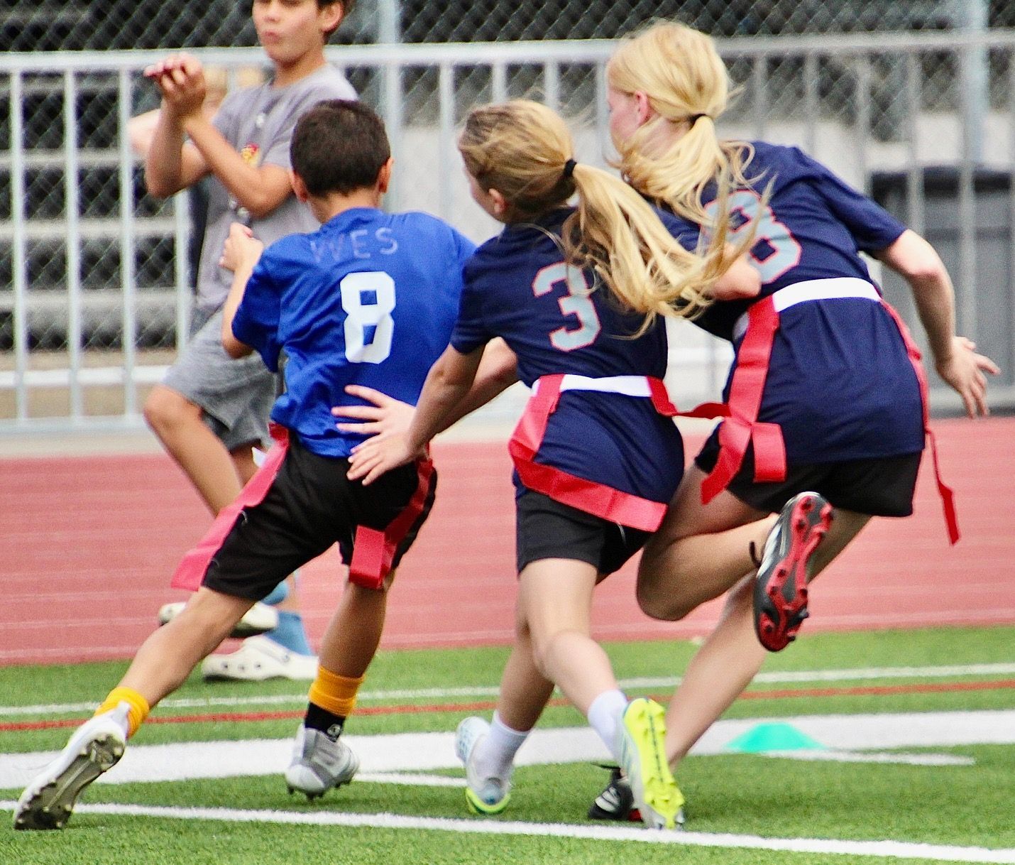 Children in blue jerseys running on a track toward a goal during a sports game